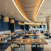 Elegant dining area featuring wooden tables, blue chairs, warm lighting, and woven pendant lamps. Modern decor with soft textures.