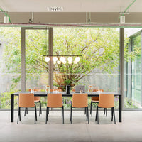 Modern black dining table with six tan chairs, set against a bright green garden backdrop.