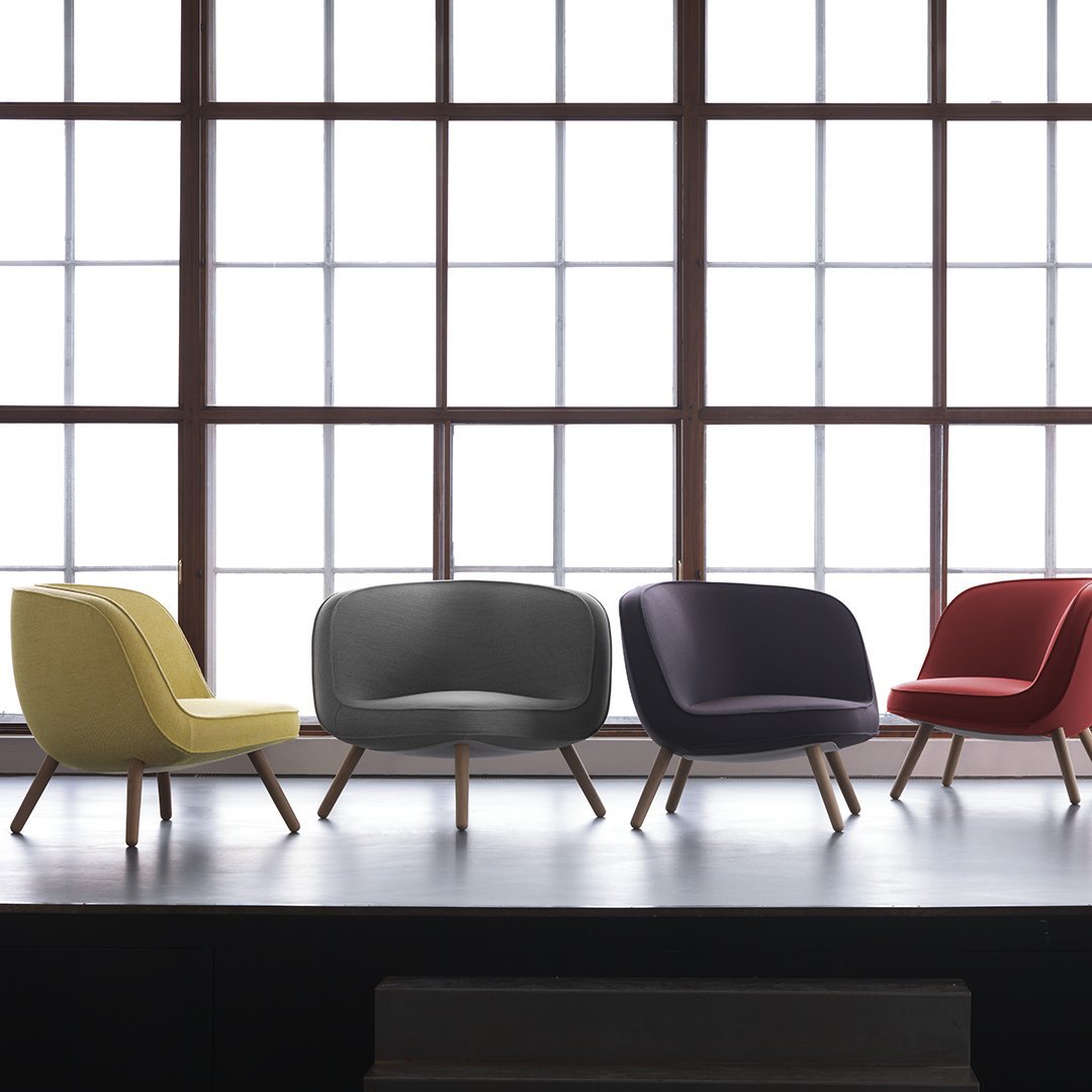 Colorful modern chairs in yellow, gray, purple, and red with sleek wooden legs against a bright window backdrop.