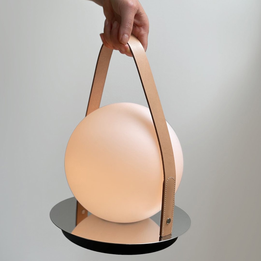 Soft beige round lamp with a light wood handle and sleek black base, showcasing a modern and minimalist design.