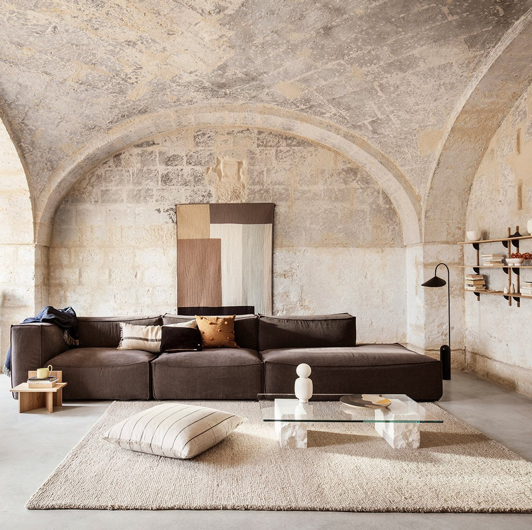 Brown sectional sofa with neutral cream and beige accents; textured beige rug and soft pillows add warmth.