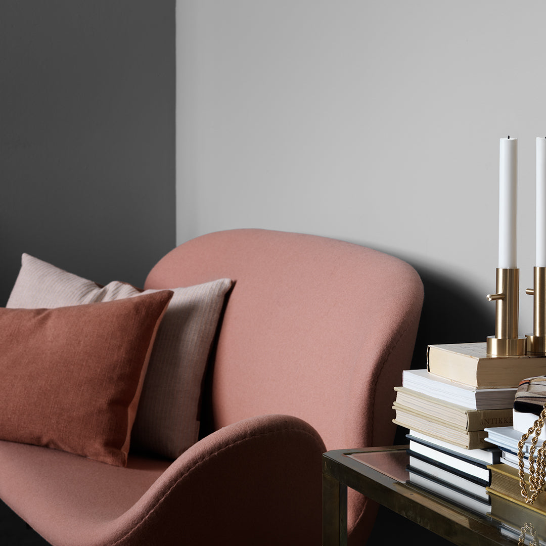 Soft pink chair with neutral cushions, gray and light gray wall backdrop, and stacked books with gold accents.