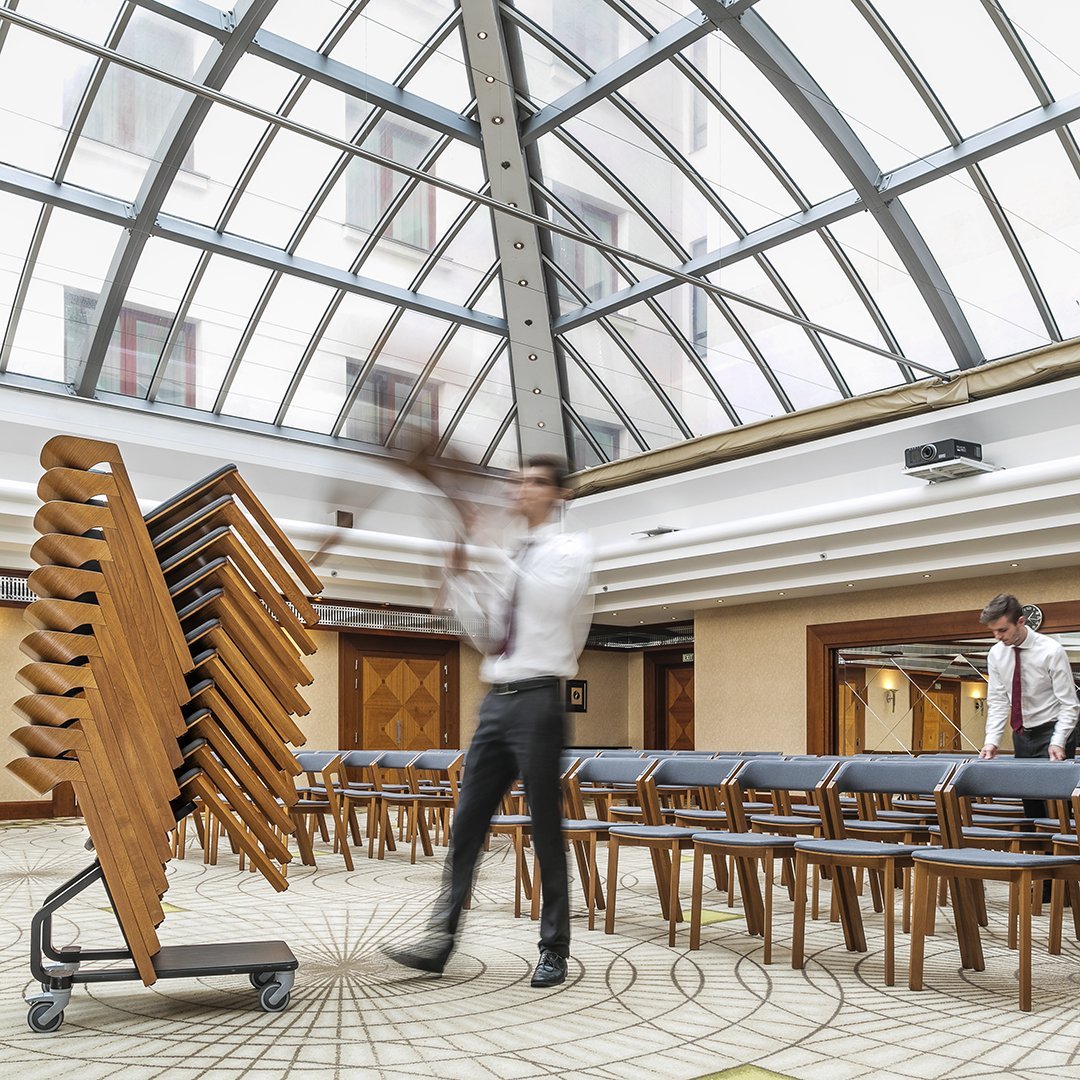Wooden chairs with rich brown tones, arranged in neat rows against a light, patterned floor and bright, airy ceiling.
