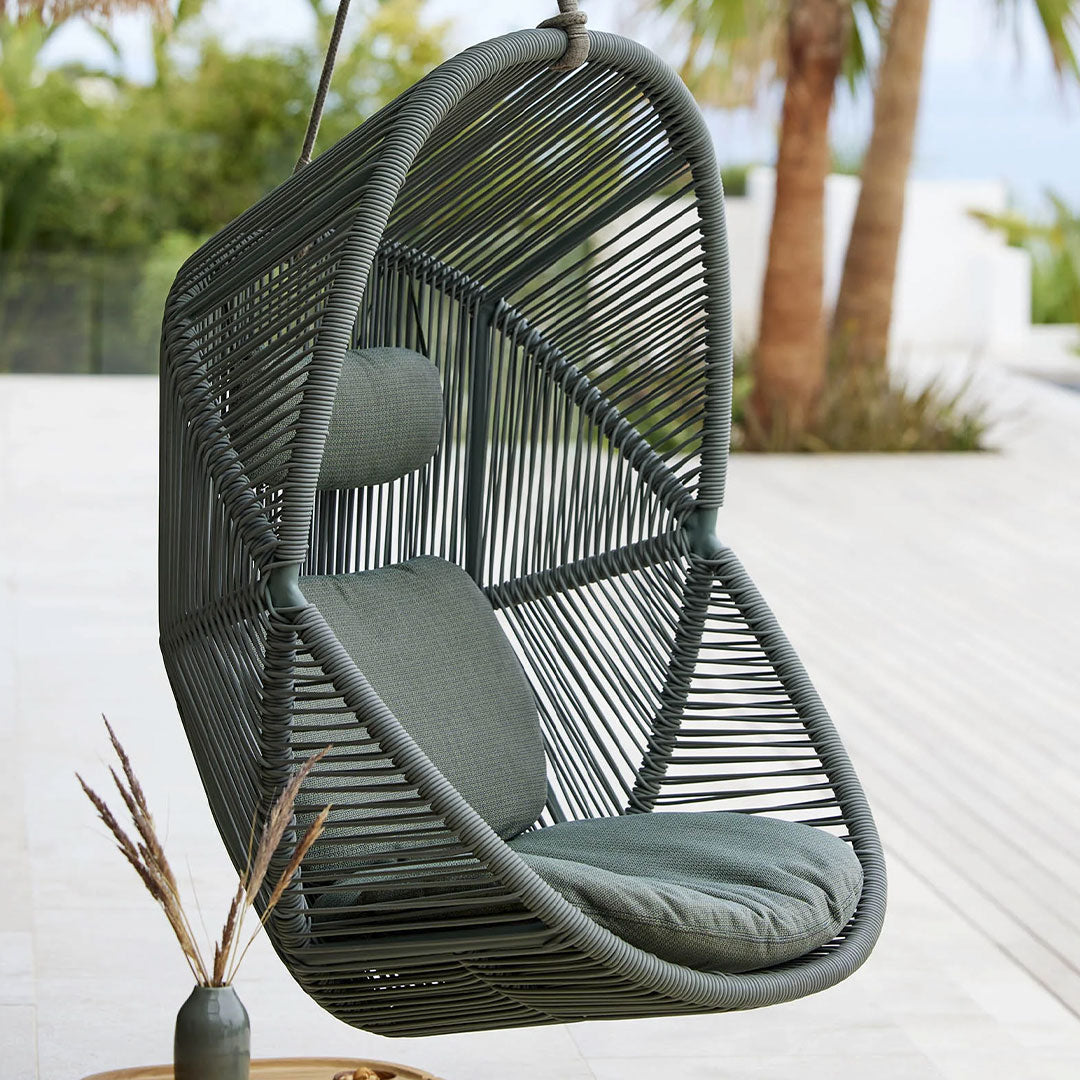 "Modern hanging chair in dark green with sleek geometric patterns and plush gray cushions for outdoor relaxation."