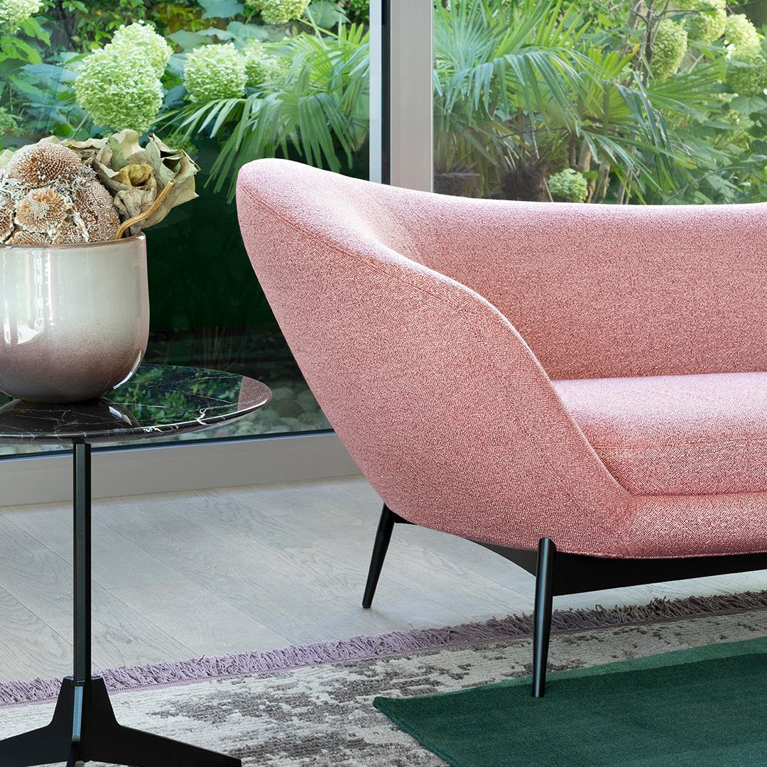 Pink textured chair with sleek black legs, set against green foliage and a stylish black glass table.