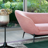 Pink textured chair with sleek black legs, set against green foliage and a stylish black glass table.