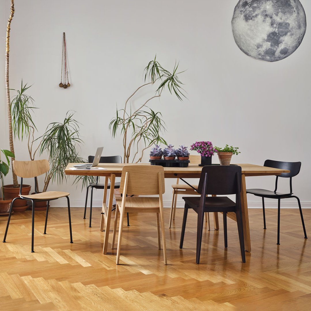 Stylish mix of natural wood tones and black chairs; elegant greenery adds vibrant touches to a minimalist dining space.