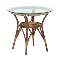 Round rattan side table with a natural brown finish and a clear glass top, featuring woven accents and an elegant design.