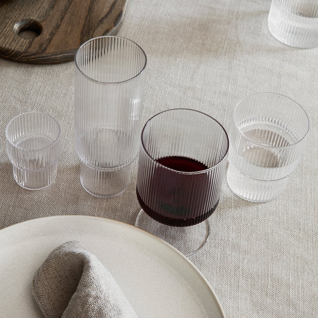 "Textured clear glass drinkware set with ribbed patterns, featuring various sizes on a neutral table setting."