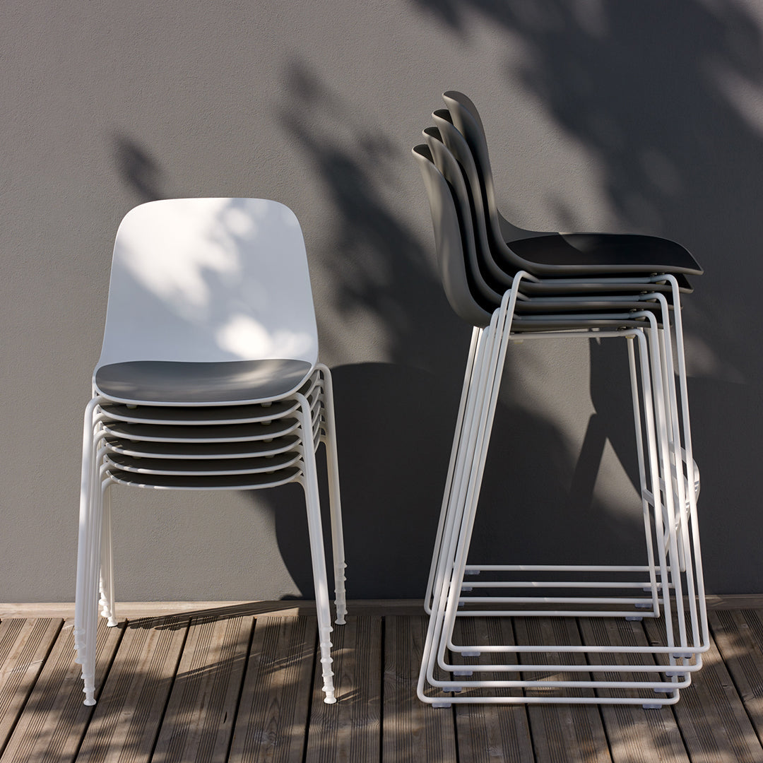 Stacked chairs in white and black against a gray wall, featuring sleek, modern designs and smooth surfaces.
