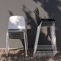 Stacked chairs in white and black against a gray wall, featuring sleek, modern designs and smooth surfaces.
