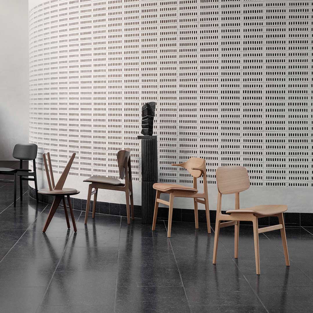 Stylish wooden chairs in varied natural finishes: light wood, dark brown, and black against a minimalistic textured wall.