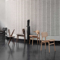 Stylish wooden chairs in varied natural finishes: light wood, dark brown, and black against a minimalistic textured wall.