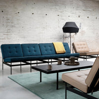 Modern sectional sofa in teal with button tufting, complemented by a mustard throw, set against a neutral backdrop.