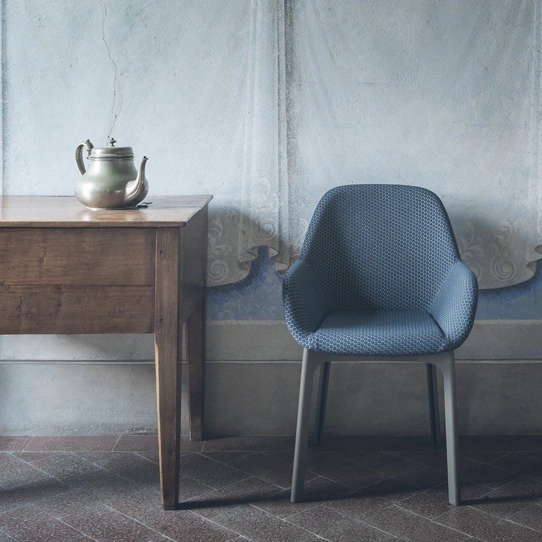 Blue upholstered chair with sleek lines, positioned beside a rustic wooden table against a textured wall backdrop.