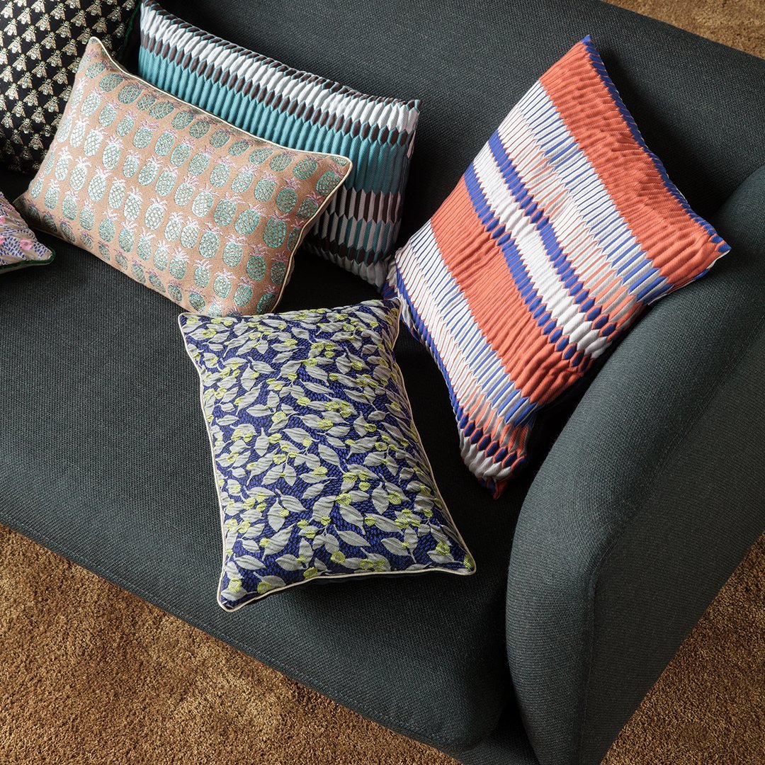 Colorful decorative pillows featuring geometric, floral, and striped patterns in vibrant shades on a modern couch.