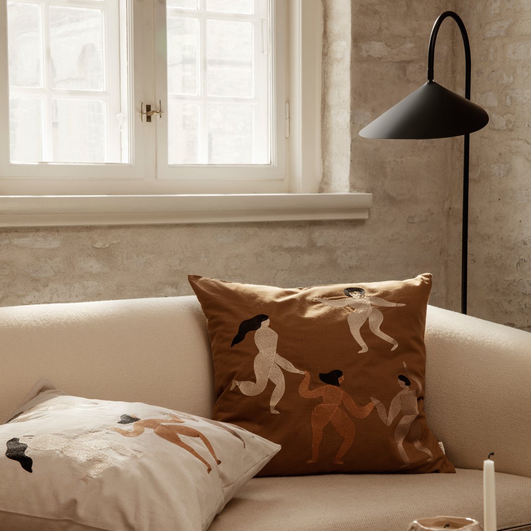 Decorative throw pillows featuring earthy tones and abstract human figures against a neutral background.