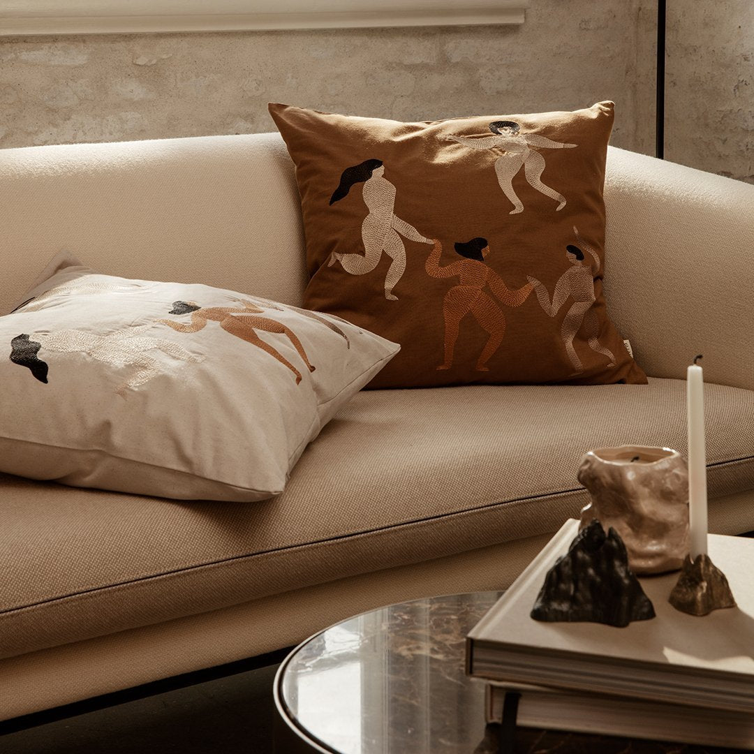 "Decorative cushions in earthy tones with abstract patterns, featuring figures in elegant poses on a stylish sofa."