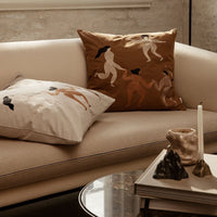 "Decorative cushions in earthy tones with abstract patterns, featuring figures in elegant poses on a stylish sofa."