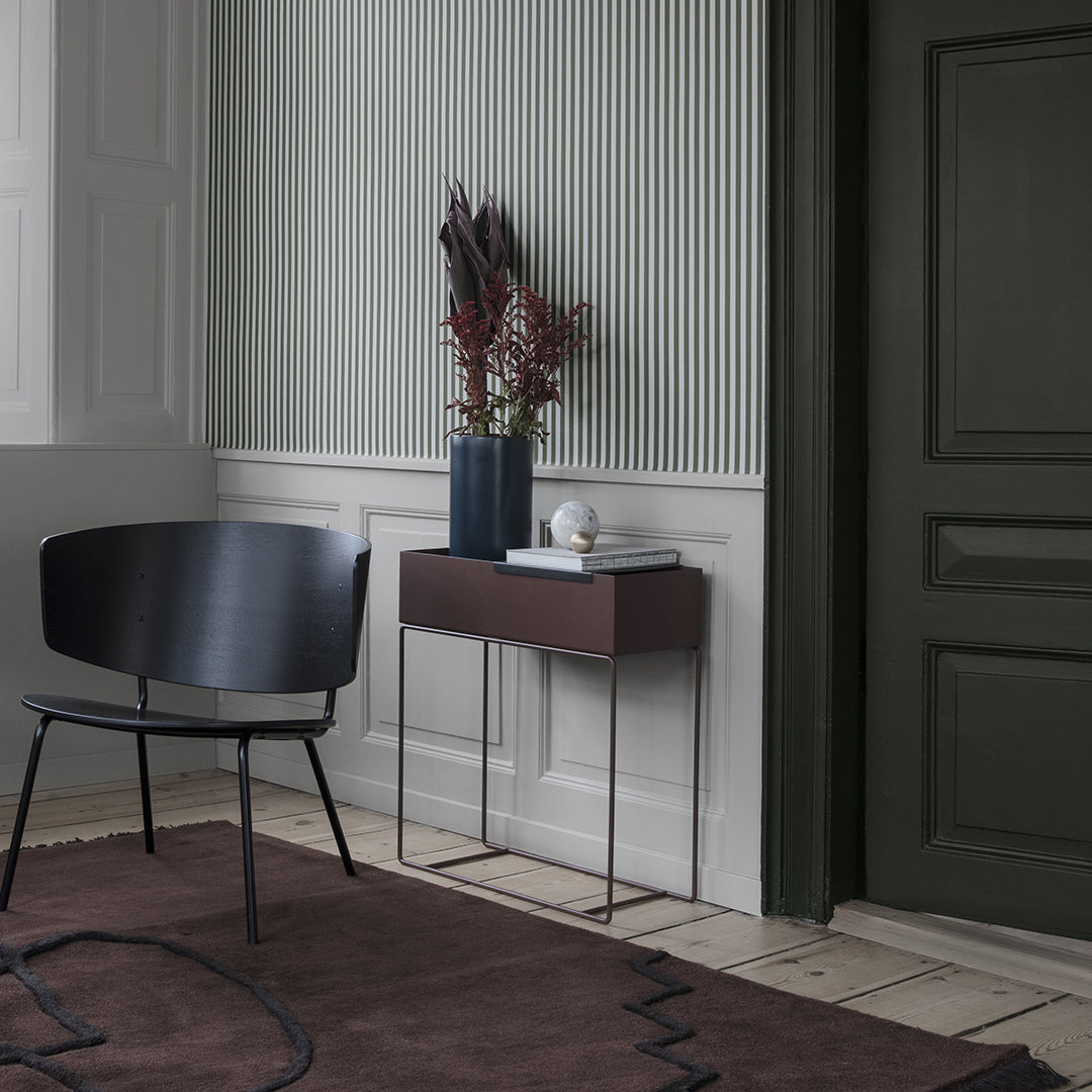 Black chair with sleek lines, dark wood console table, and earthy brown rug featuring geometric patterns against soft gray walls.