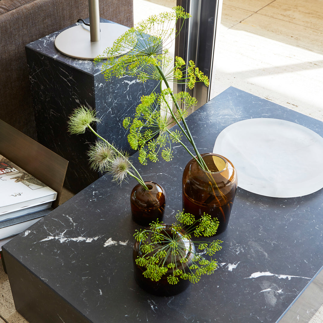 "Three amber glass vases on a black marble table, showcasing earthy tones and organic shapes with greenery accents."