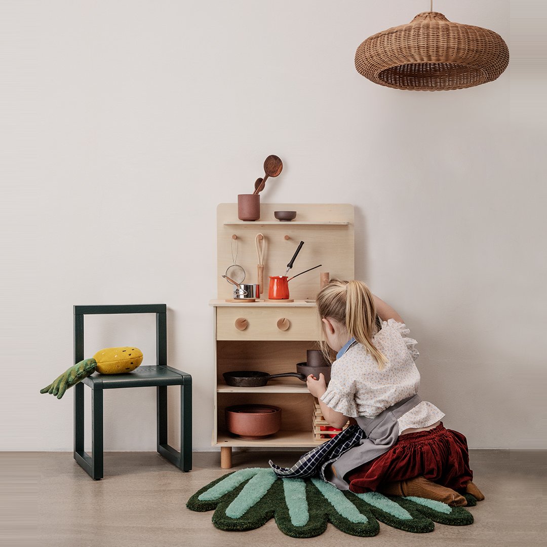 Colorful play kitchen with wooden shelves, green leaf-shaped rug, and earthy tones in pots and decor.