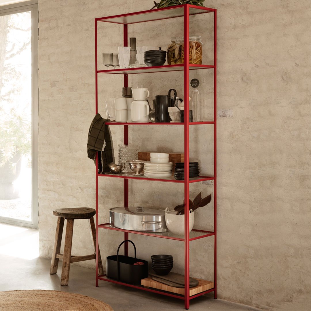 Red metal shelving unit with clear glass shelves, showcasing a minimalist style in an industrial setting.
