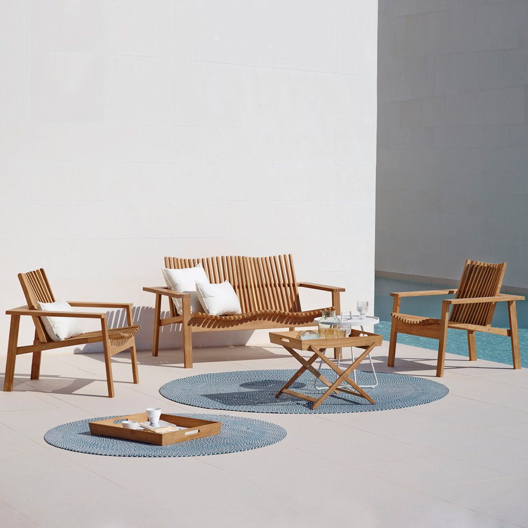 "Natural wood outdoor seating with white cushions on blue circular rugs, set against a minimalist white background."