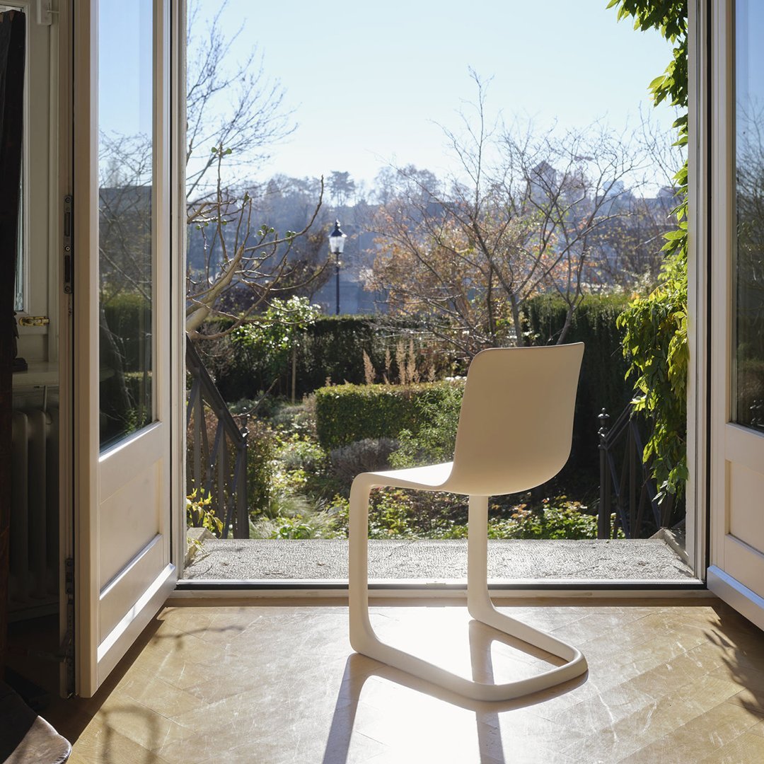 Modern white chair with a sleek, minimalist design, set against a bright outdoor view and greenery.