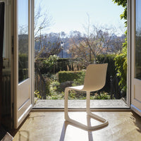 Modern white chair with a sleek, minimalist design, set against a bright outdoor view and greenery.