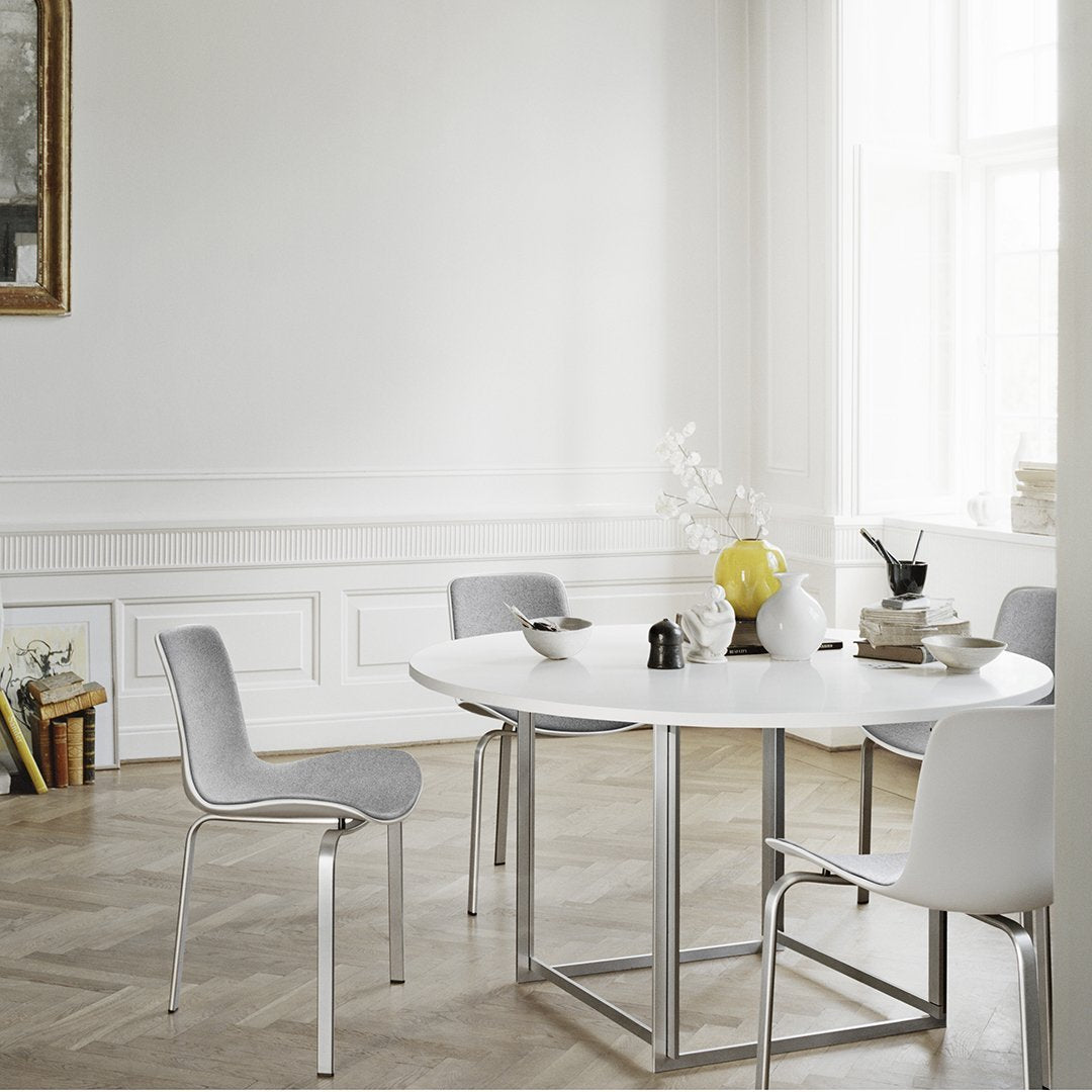 Modern round white dining table with sleek gray chairs and minimalist decor, featuring neutral tones and subtle textures.