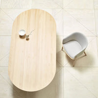 Light natural wood table with a smooth finish, paired with a soft gray upholstered chair on pale patterned flooring.