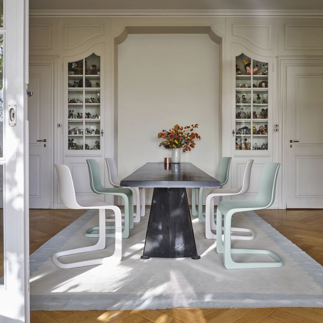Modern dining room with mint green and white chairs, black table, and neutral-toned rug, creating a stylish, minimalistic look.