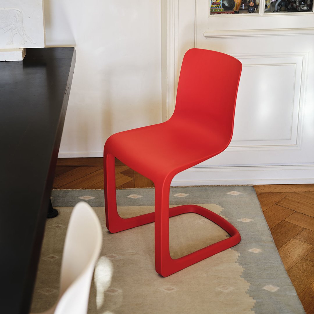 Red modern chair on a patterned rug, featuring a sleek, minimalist design with a curved base.