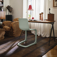 Light green minimalist chair against a textured brown rug, with soft natural light filtering through sheer curtains.