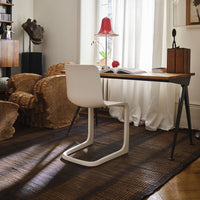 Modern white chair with a sleek design, set against a textured brown rug, complemented by warm wood tones and golden accents.