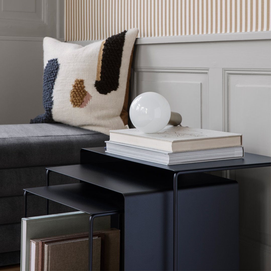 Decorative cushion with abstract patterns in cream, navy, brown, and rust on a gray sofa beside a sleek black side table.