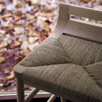 Natural woven chair seat featuring a geometric pattern in earthy beige tones against a blurred autumn background.