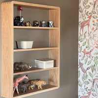 Light wood shelf with colorful animal figurines atop a muted beige wall and a soft, vibrant nature-patterned wallpaper.