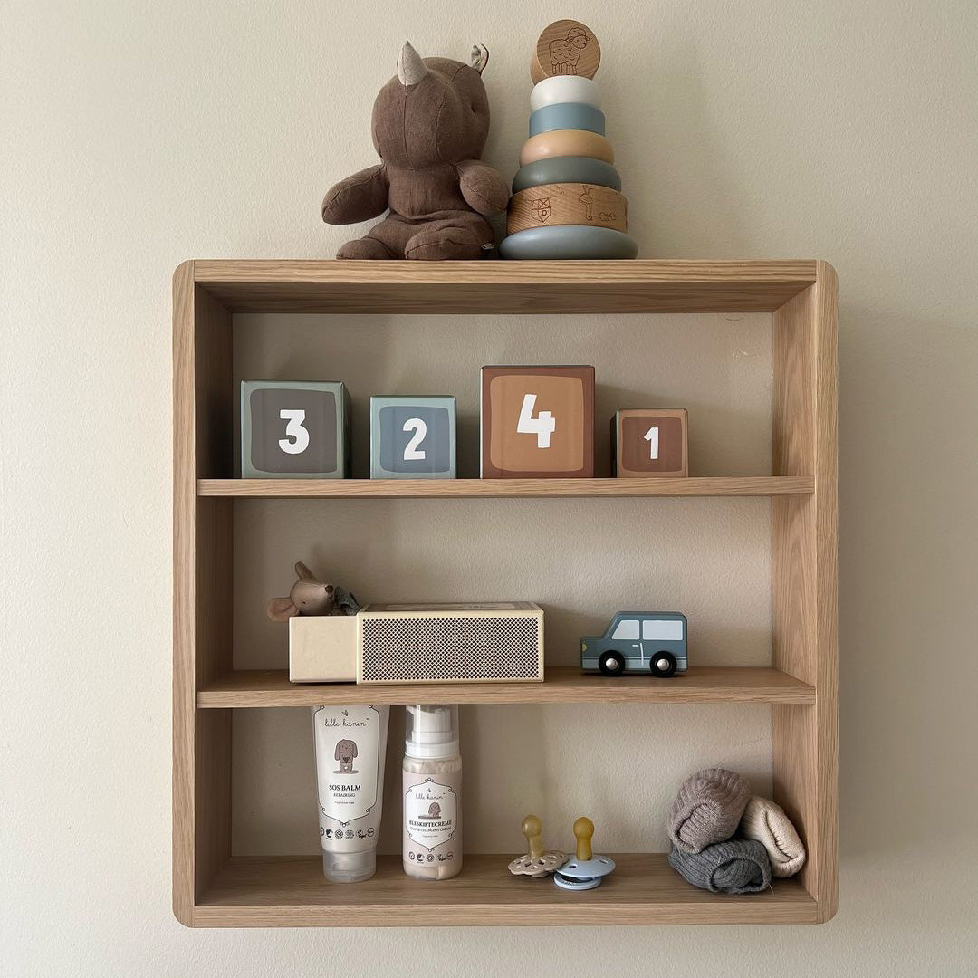 Wooden shelf with soft pastel colors, featuring blue, brown, and cream blocks, plush toys, and neutral-toned accessories.