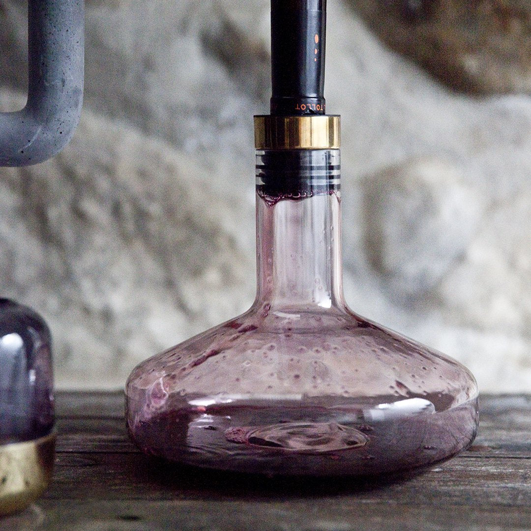 Elegant purple glass bottle with bubbles and a sleek black and gold neck, set against a rustic background.