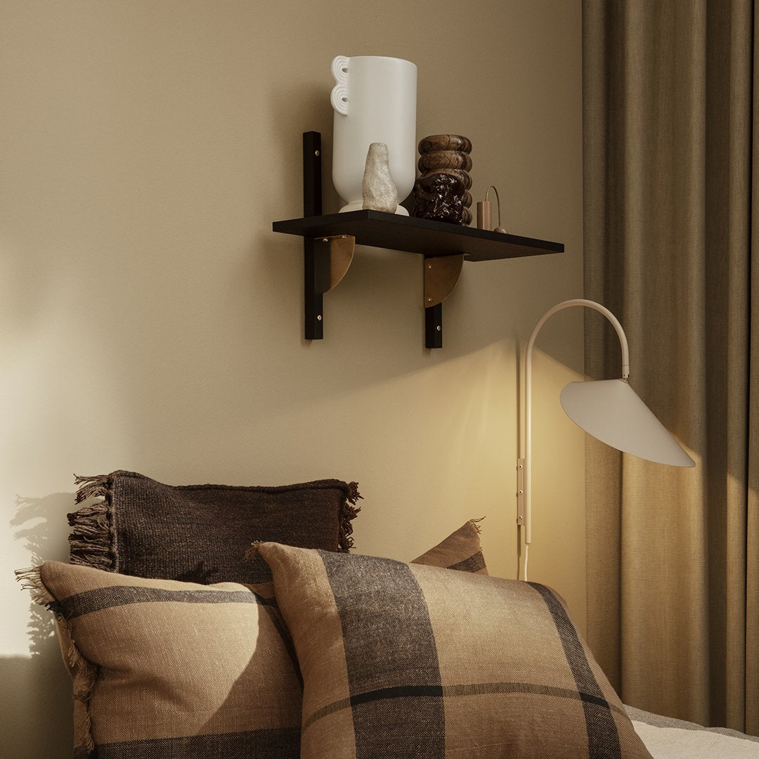 Brown plaid pillows on a bed, with a dark wooden shelf displaying a white vase, set against a warm beige wall.