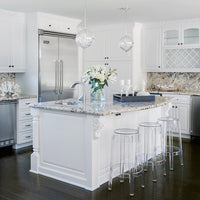 Elegant white kitchen with granite countertops, clear stools, and intricate backsplash patterns in neutral tones.