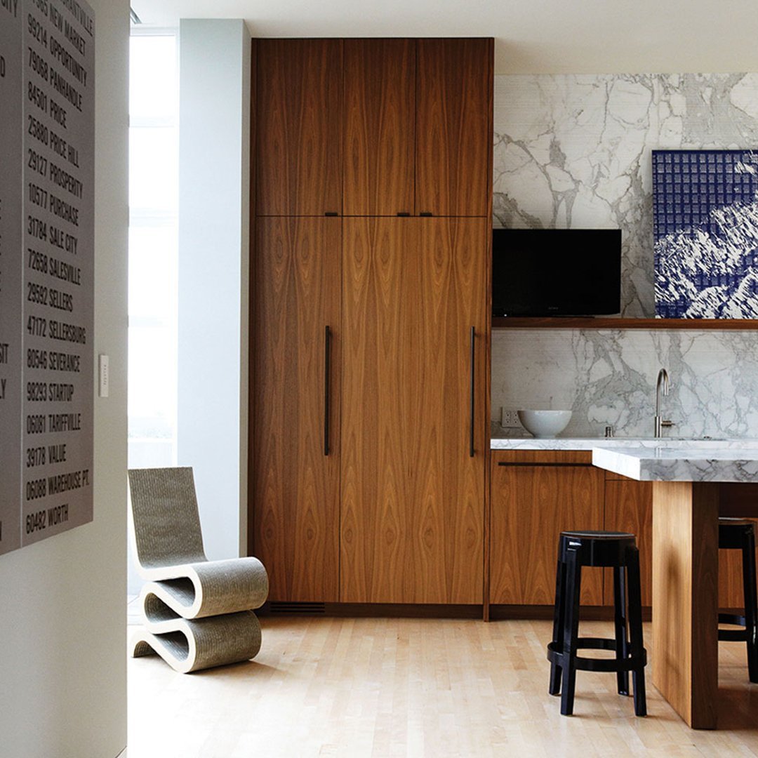 Modern kitchen featuring wood tones, white marble, and navy blue accents with sleek black bar stools.