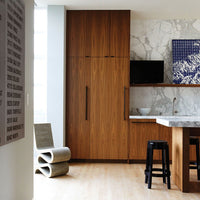 Modern kitchen featuring wood tones, white marble, and navy blue accents with sleek black bar stools.