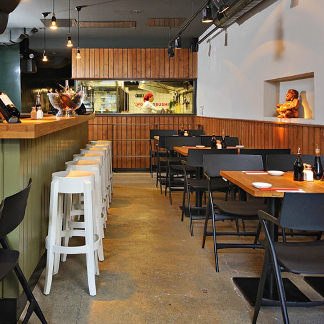 Stylish restaurant interior featuring white and black stools, wooden accents, and concrete flooring.