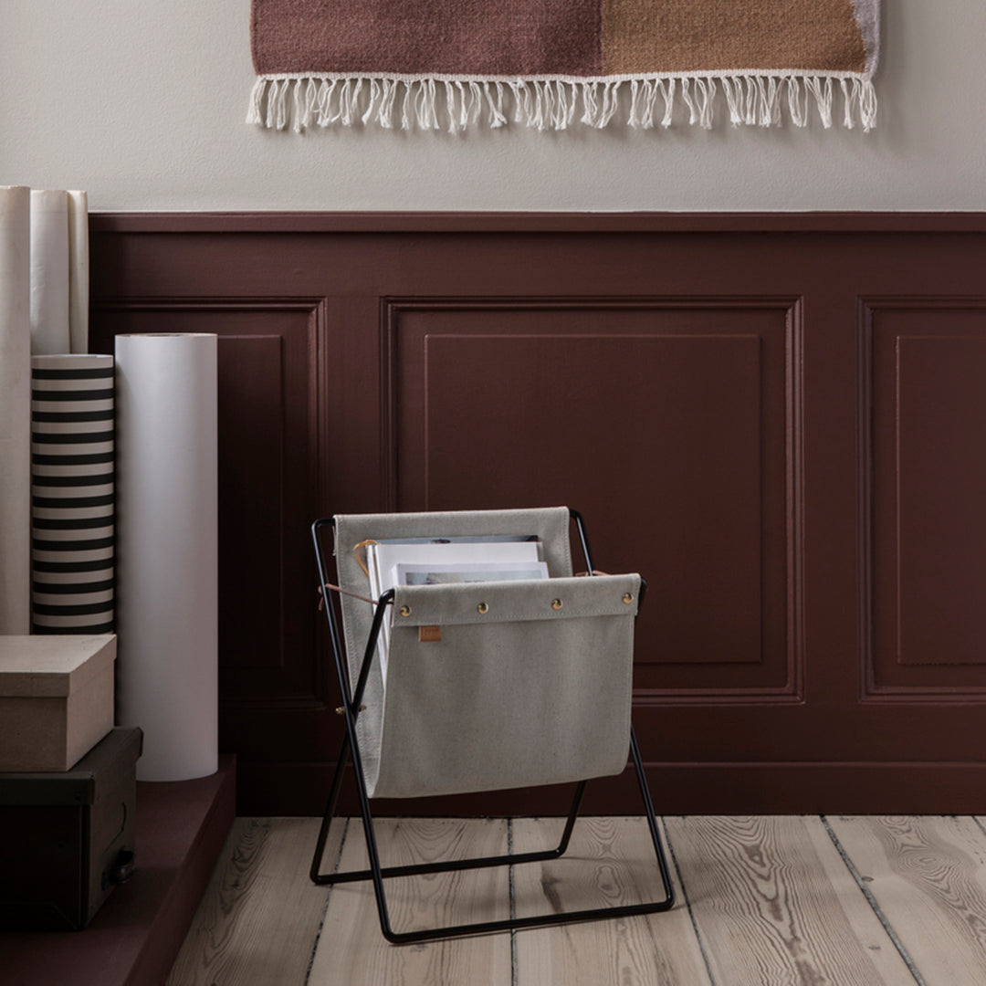 Neutral gray storage bag with black frame against a rich burgundy wall, complemented by a warm, textured blanket.