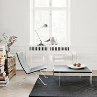 Modern black chair and square table atop a textured black rug, surrounded by white walls and natural light.