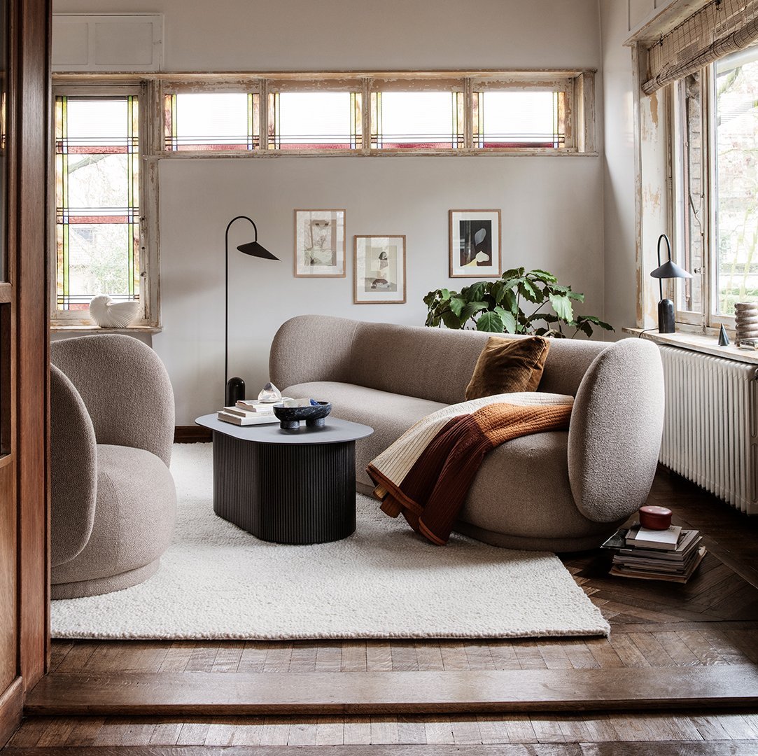 Beige rounded sofa and armchair with a brown throw, black coffee table, and light cream rug in a cozy, patterned living room.