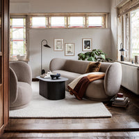Beige rounded sofa and armchair with a brown throw, black coffee table, and light cream rug in a cozy, patterned living room.